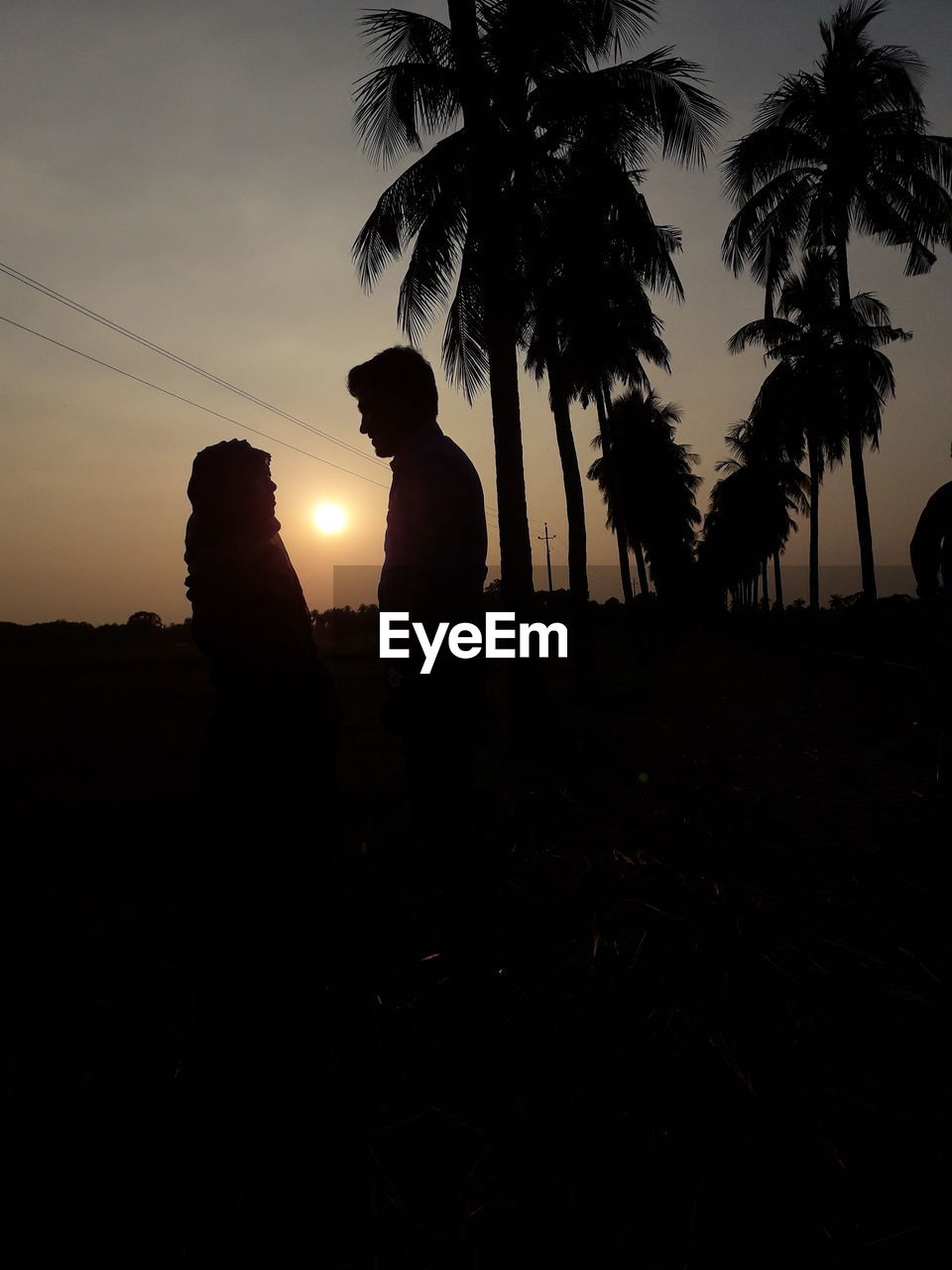 SILHOUETTE PEOPLE STANDING BY PALM TREE AGAINST SUNSET SKY