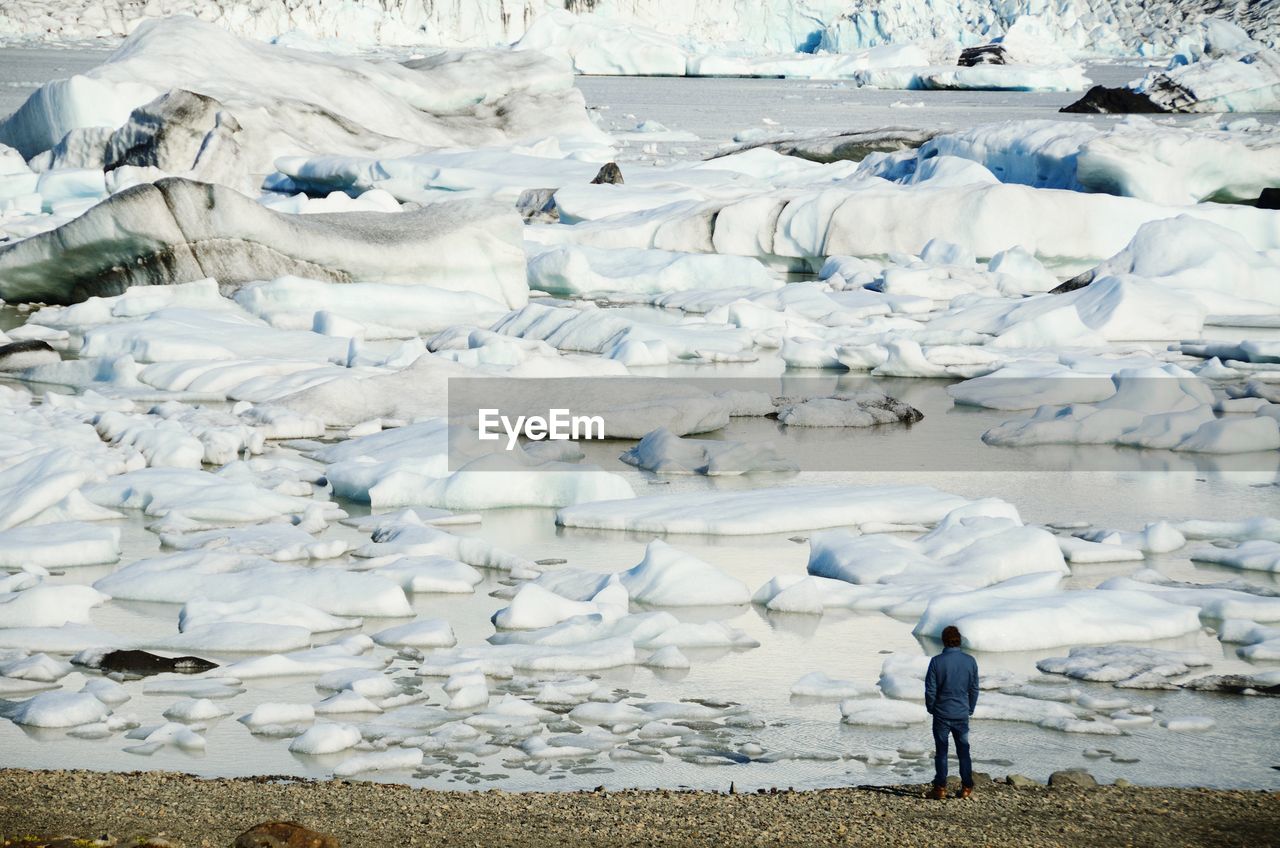 Full length rear view of man looking at icebergs in lagoon