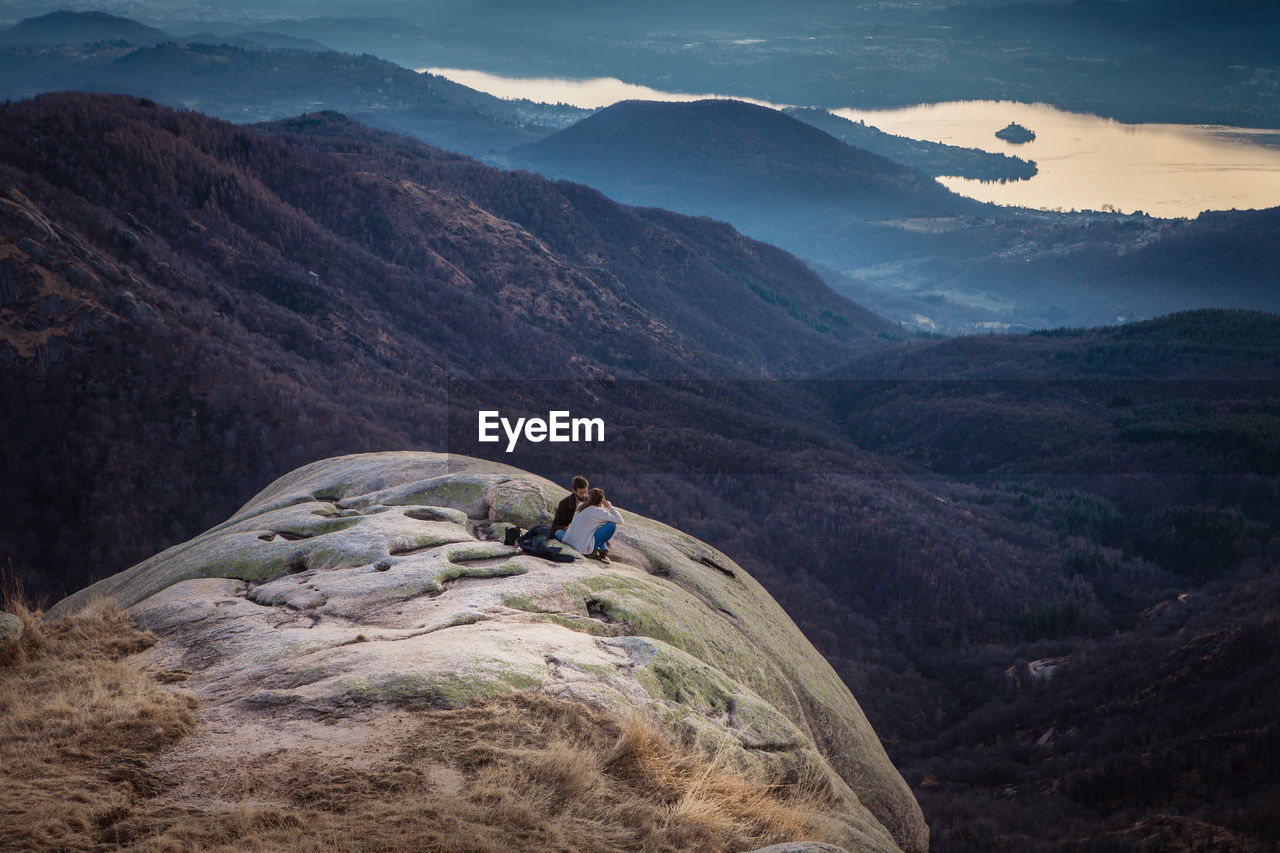 High angle view of couple sitting on rock by mountains