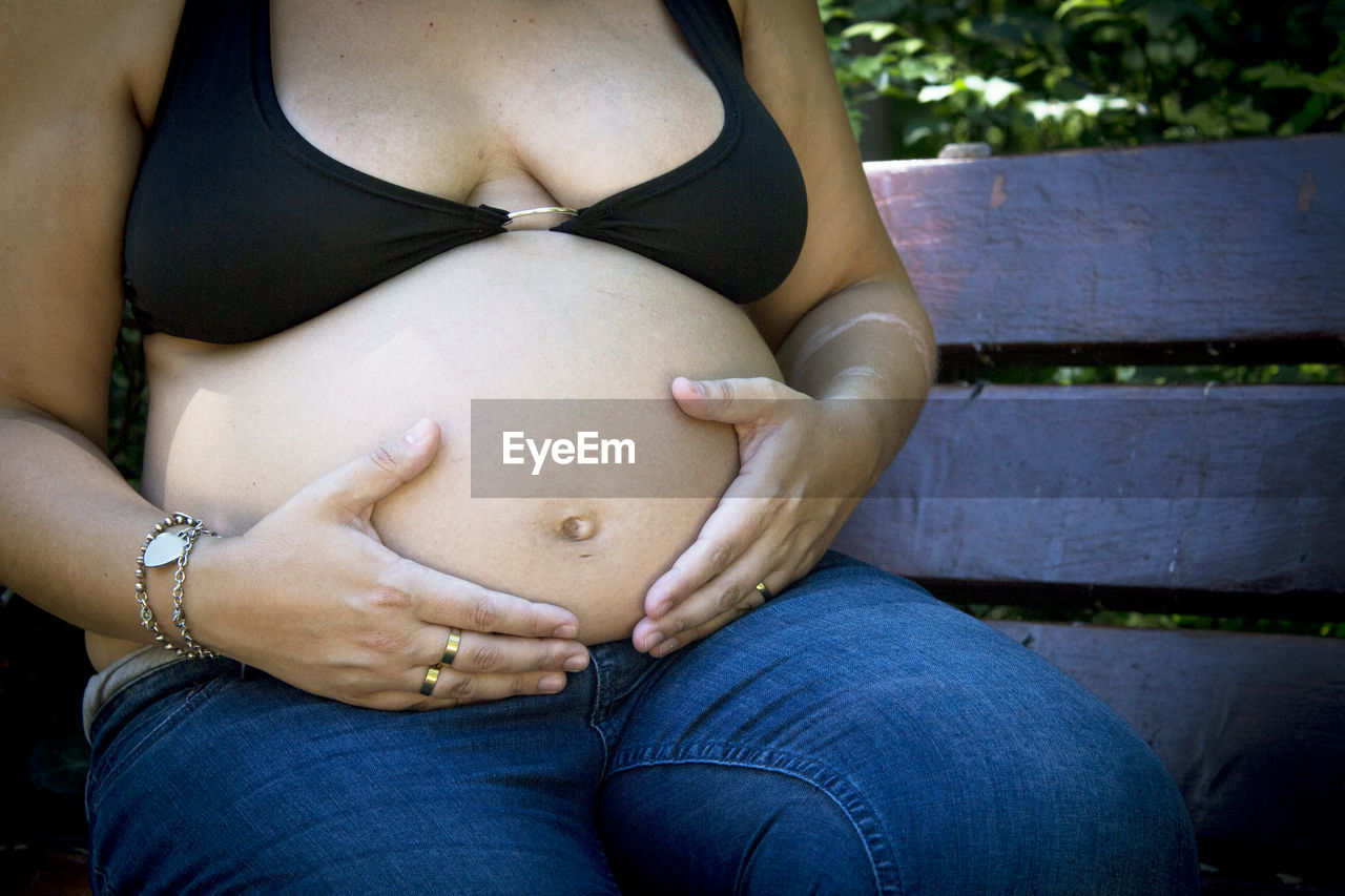 pregnant, parent, adult, anticipation, beginnings, women, midsection, human fertility, hands on stomach, female, hope, person, one person, human leg, limb, clothing, life events, child, close-up, jeans, skin, positive emotion, emotion, care, lifestyles, touching, nature, hand, sitting, love, casual clothing, holding, black hair, day, family, finger, young adult, growth, baby, photo shoot, outdoors