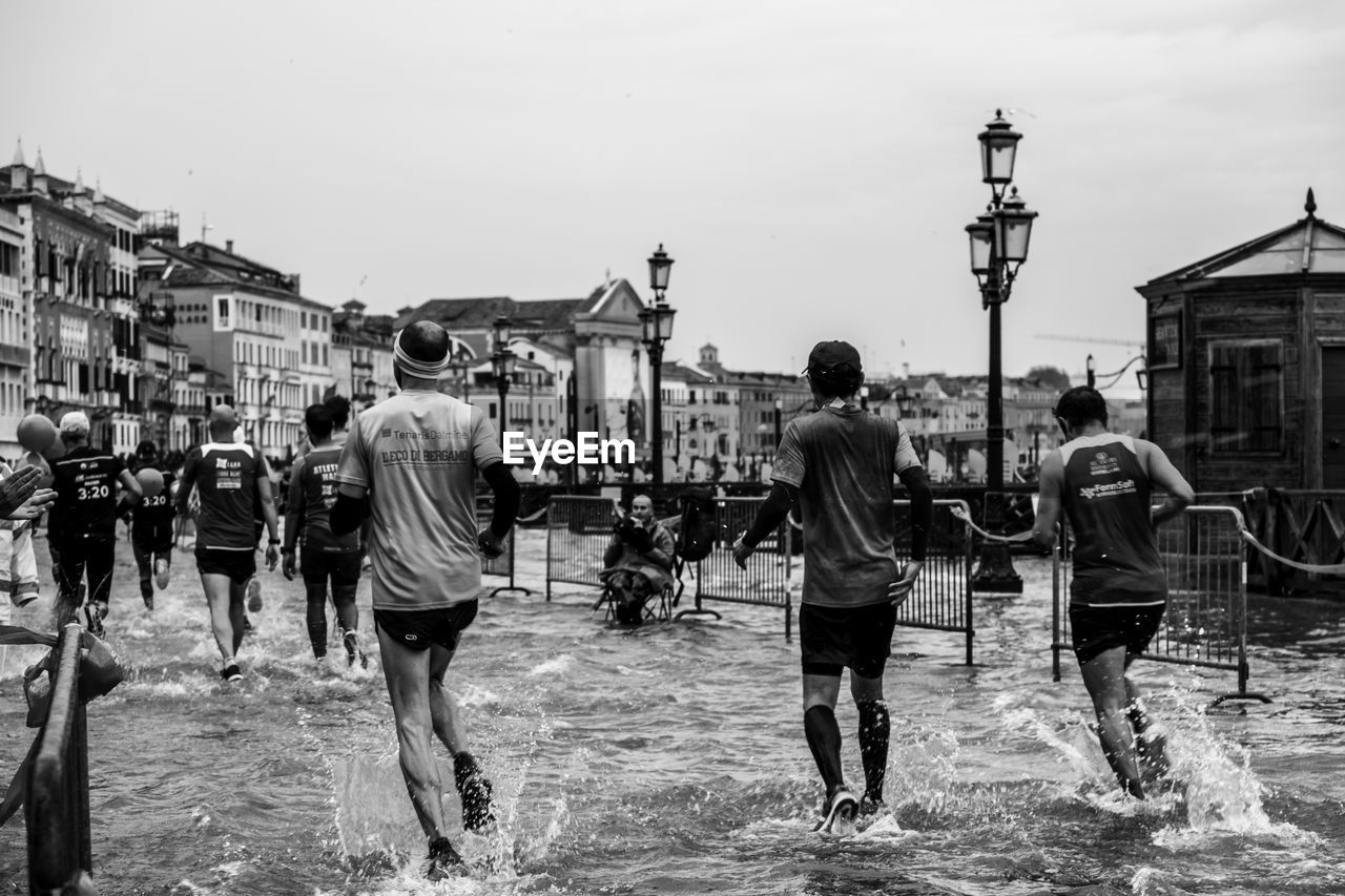 REAR VIEW OF PEOPLE WALKING ON STREET IN CITY AGAINST SKY