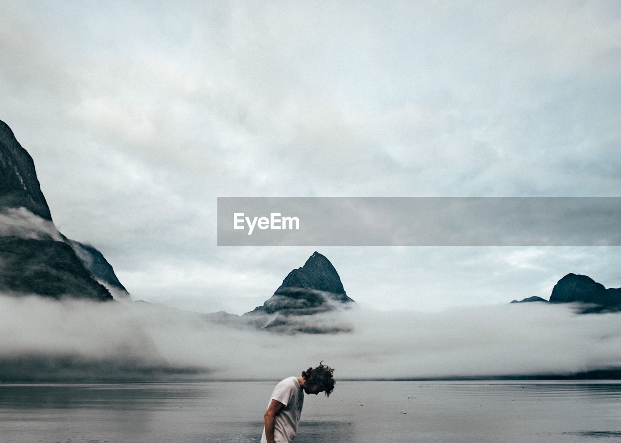 Side view of man at lakeshore against cloudy sky