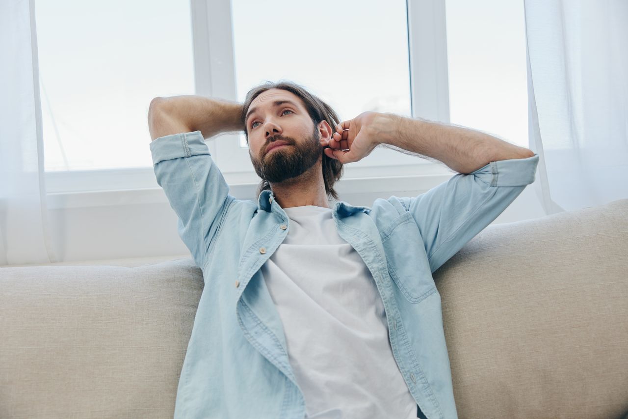 portrait of young man with arms raised sitting on bed at home