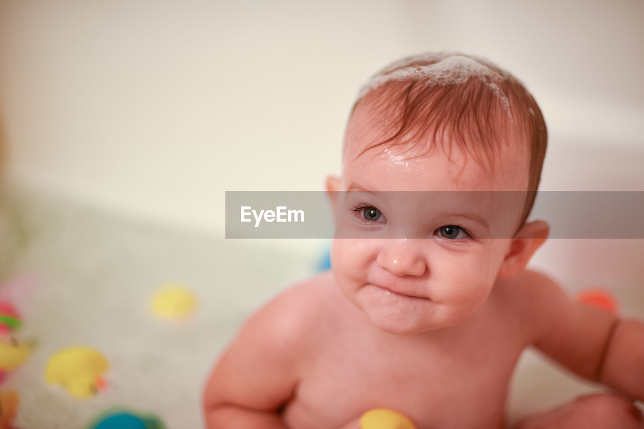 High angle view of cute wet baby girl looking away while sitting in bathtub at home