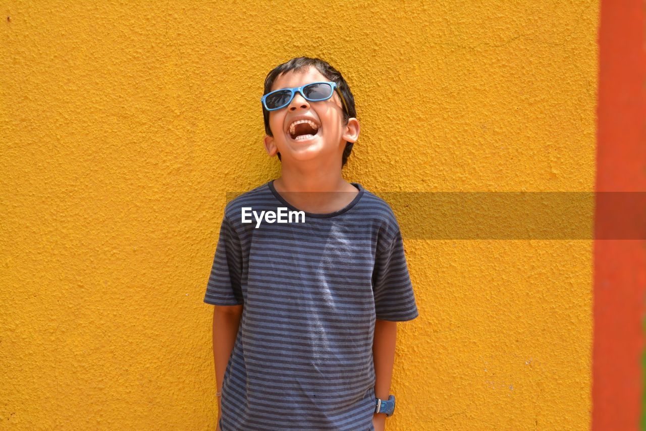 Happy boy laughing against yellow wall