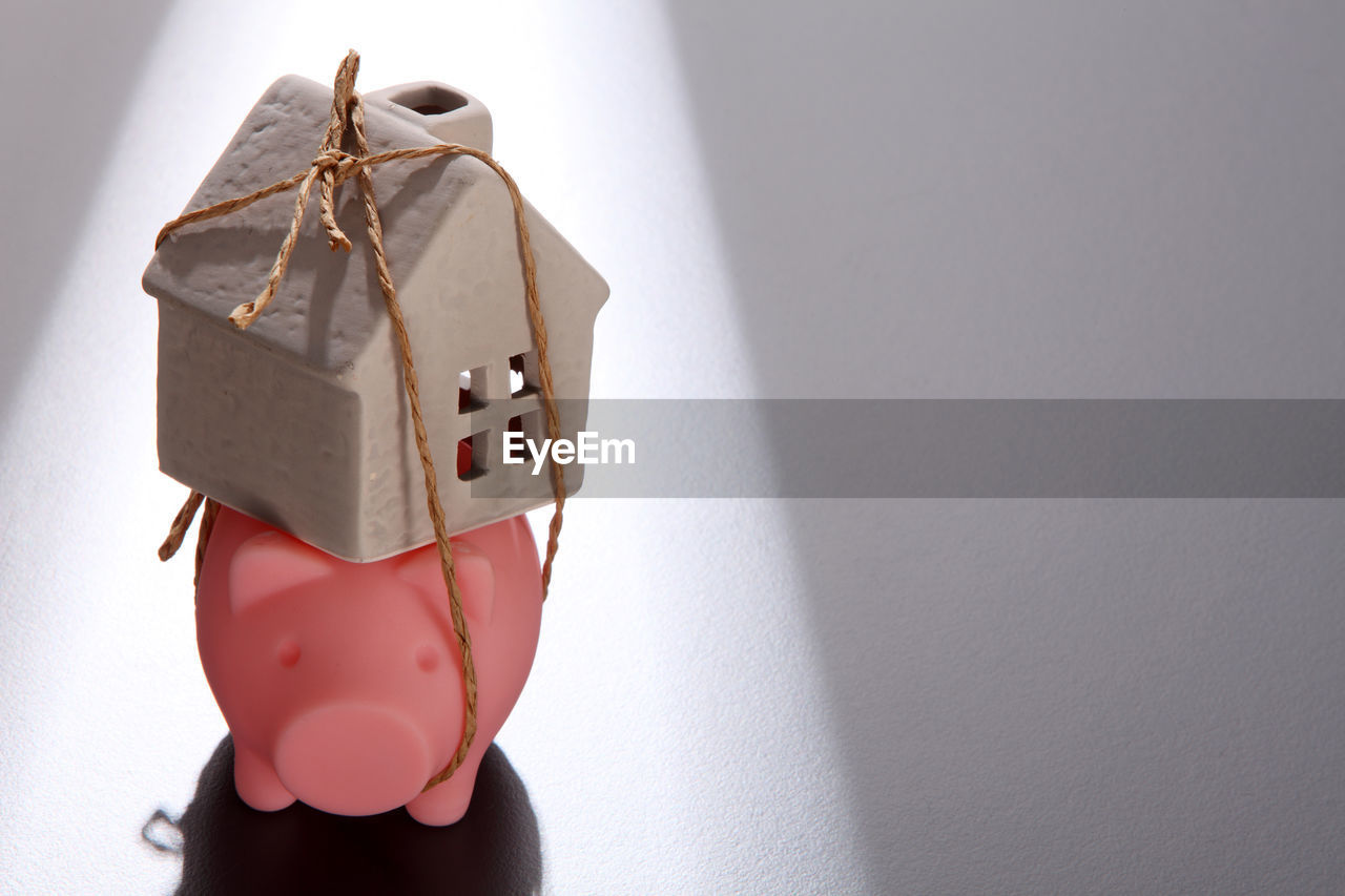 Close-up of model home tied with piggy bank on table