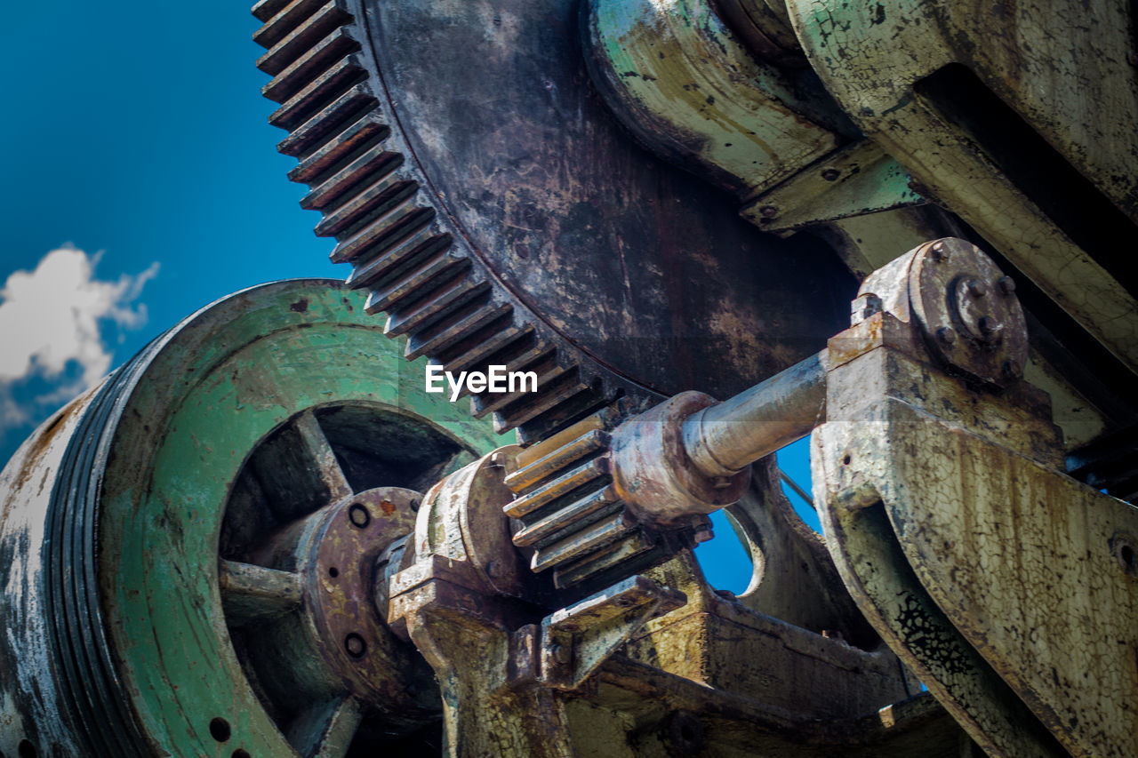 Low angle view of rusty machine part against sky