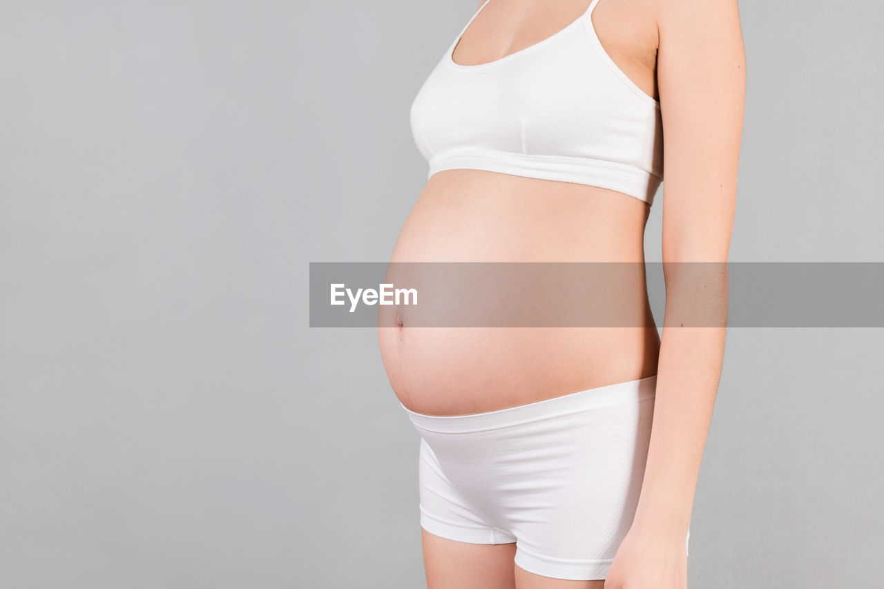 MIDSECTION OF WOMAN STANDING AGAINST WALL