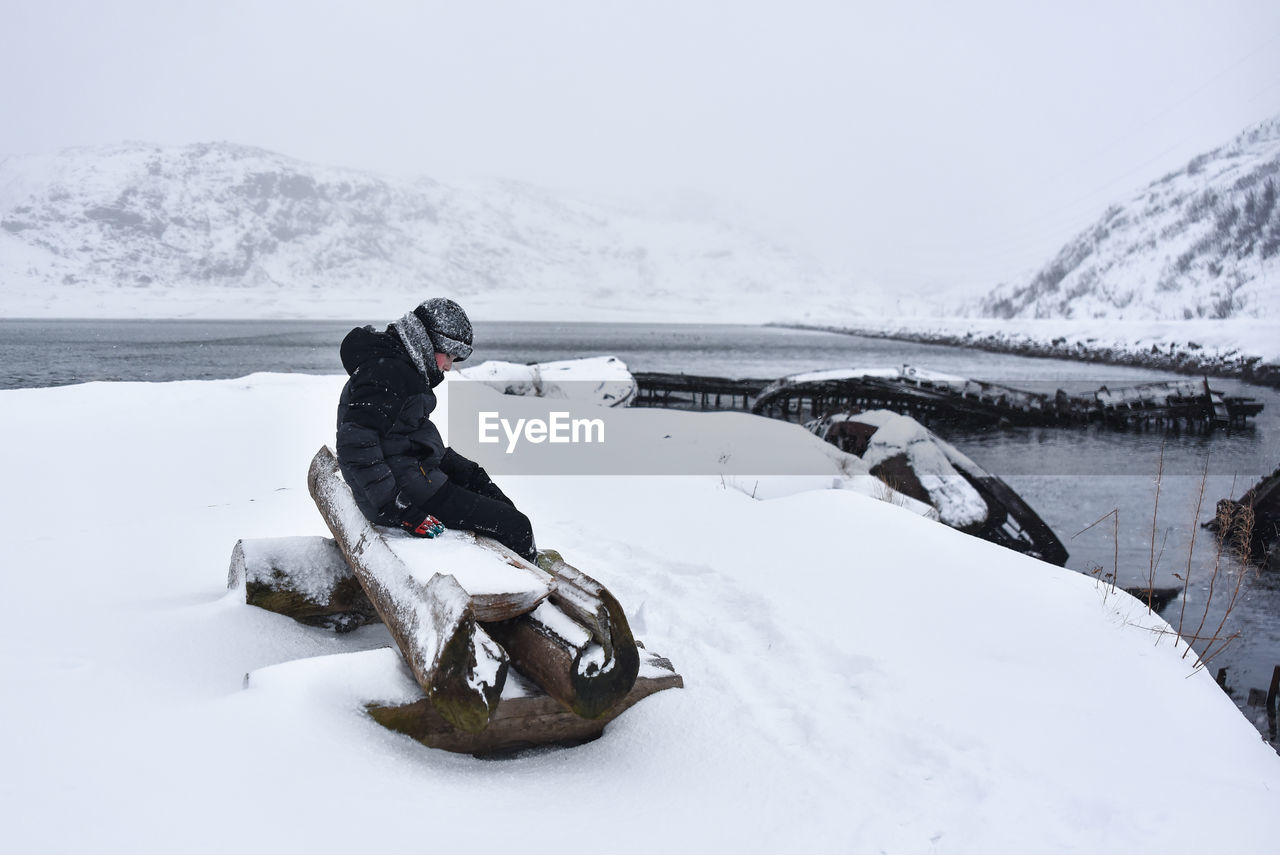 The boy sitting on a bench snow covered field