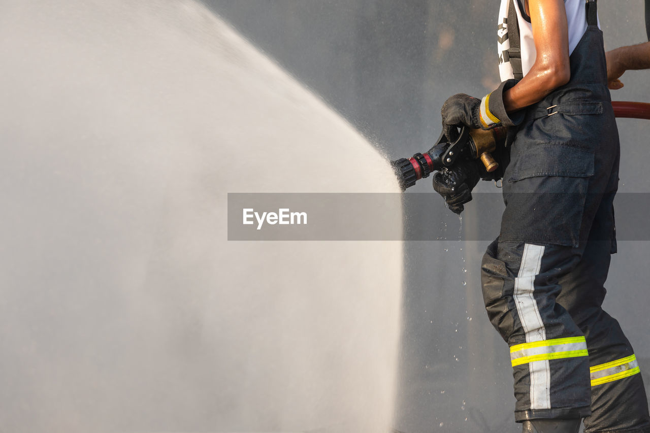 Fireman or firefighter spraying water from big water hose to prevent fire