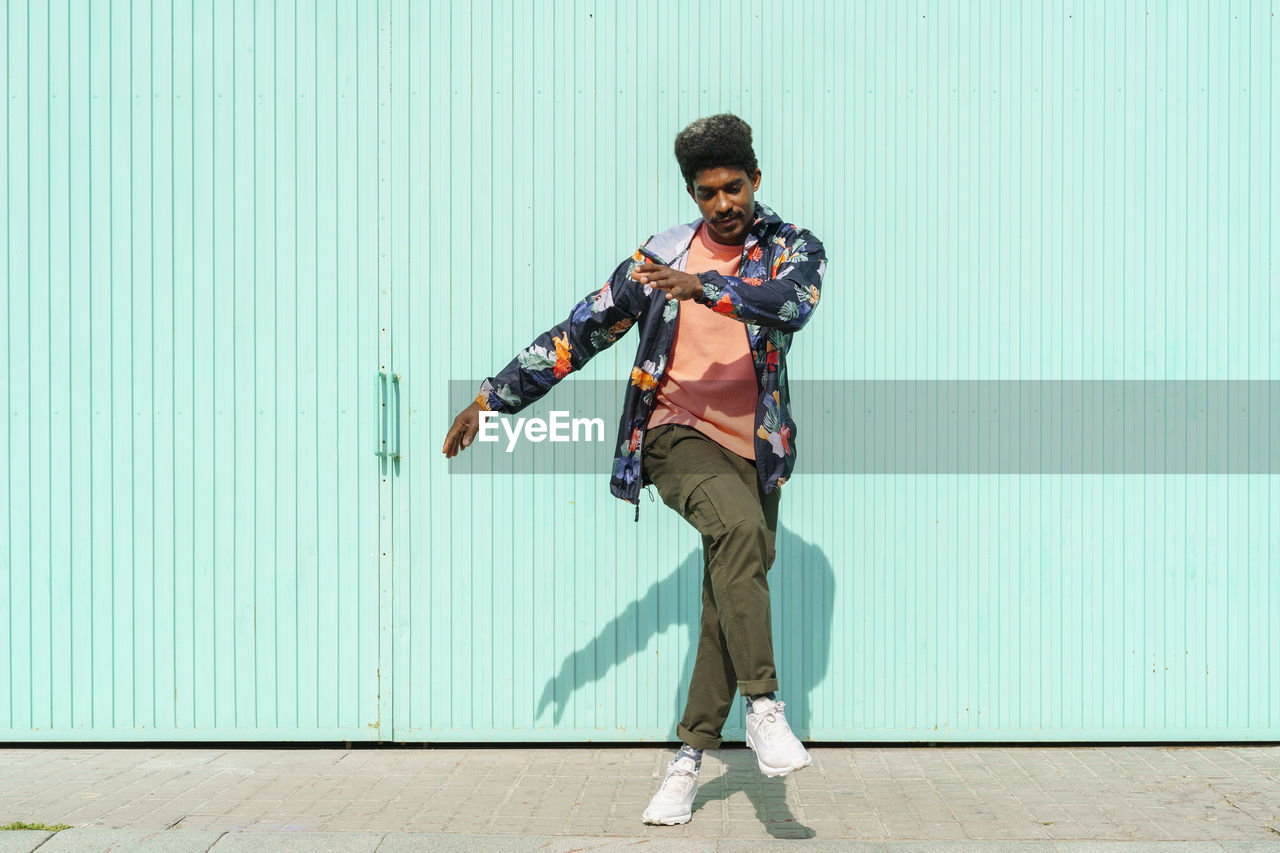 Ecstatic man dancing in front of of turquoise wall during sunny day