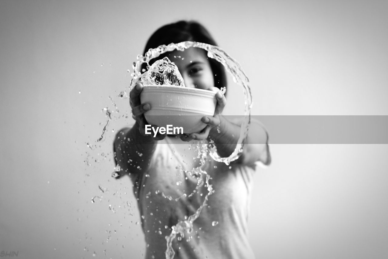 Young woman holding bowl with water against white background