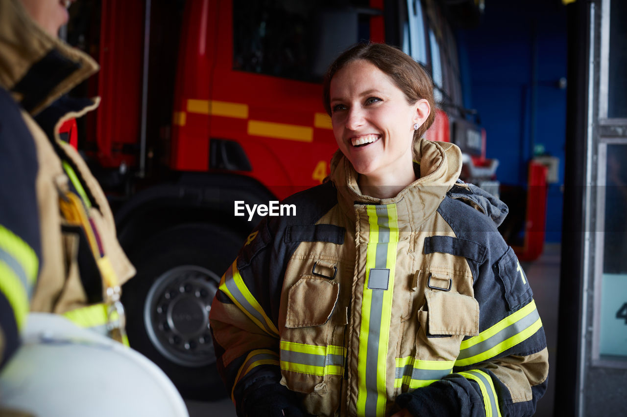 Smiling female firefighter looking at coworker while communicating in fire station