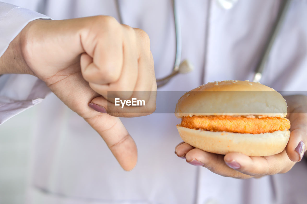 Closeup doctor hand holding unhealthy fast food burger