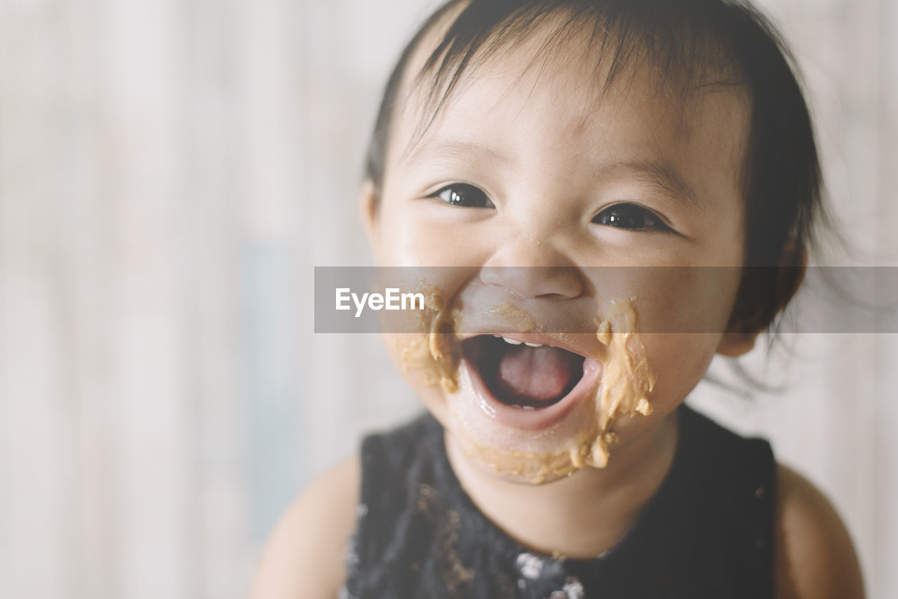 Close-up portrait of cute girl with peanut butter on face at home