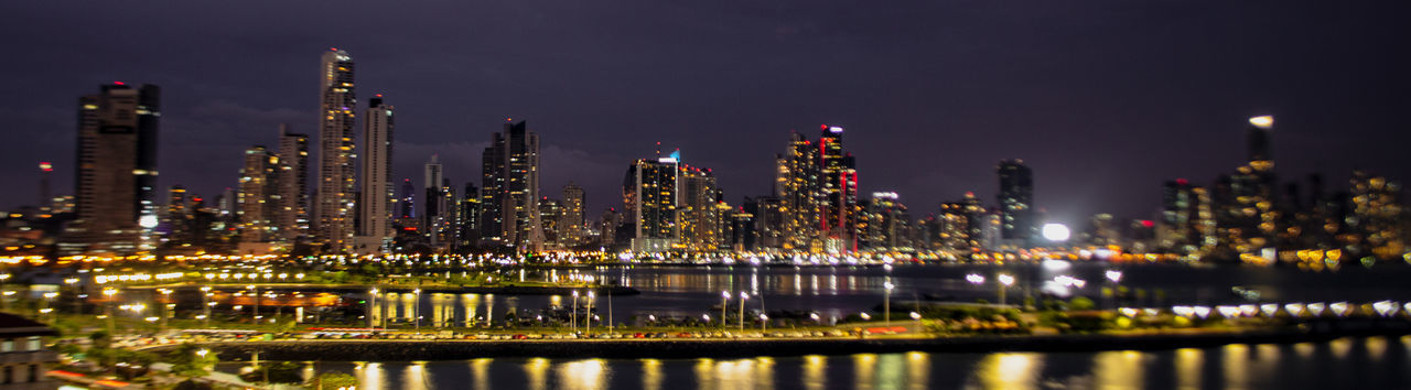 ILLUMINATED MODERN BUILDINGS BY RIVER AGAINST SKY