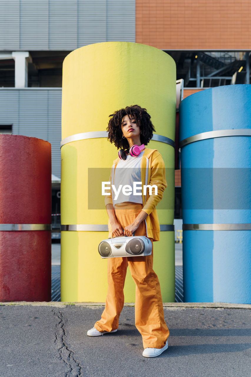 Young woman holding boom box standing in front of colorful pipes