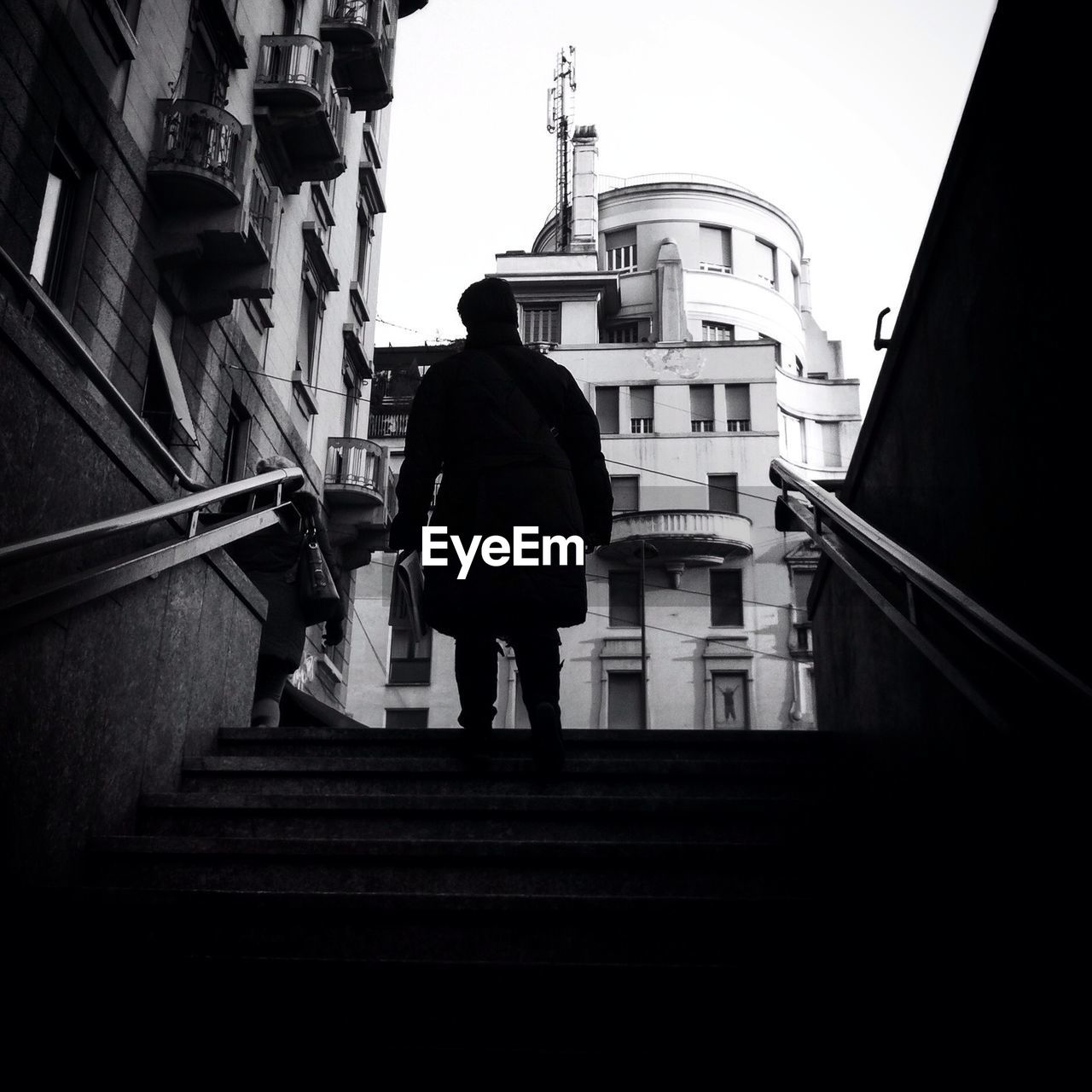 Silhouette man walking up stairs against buildings