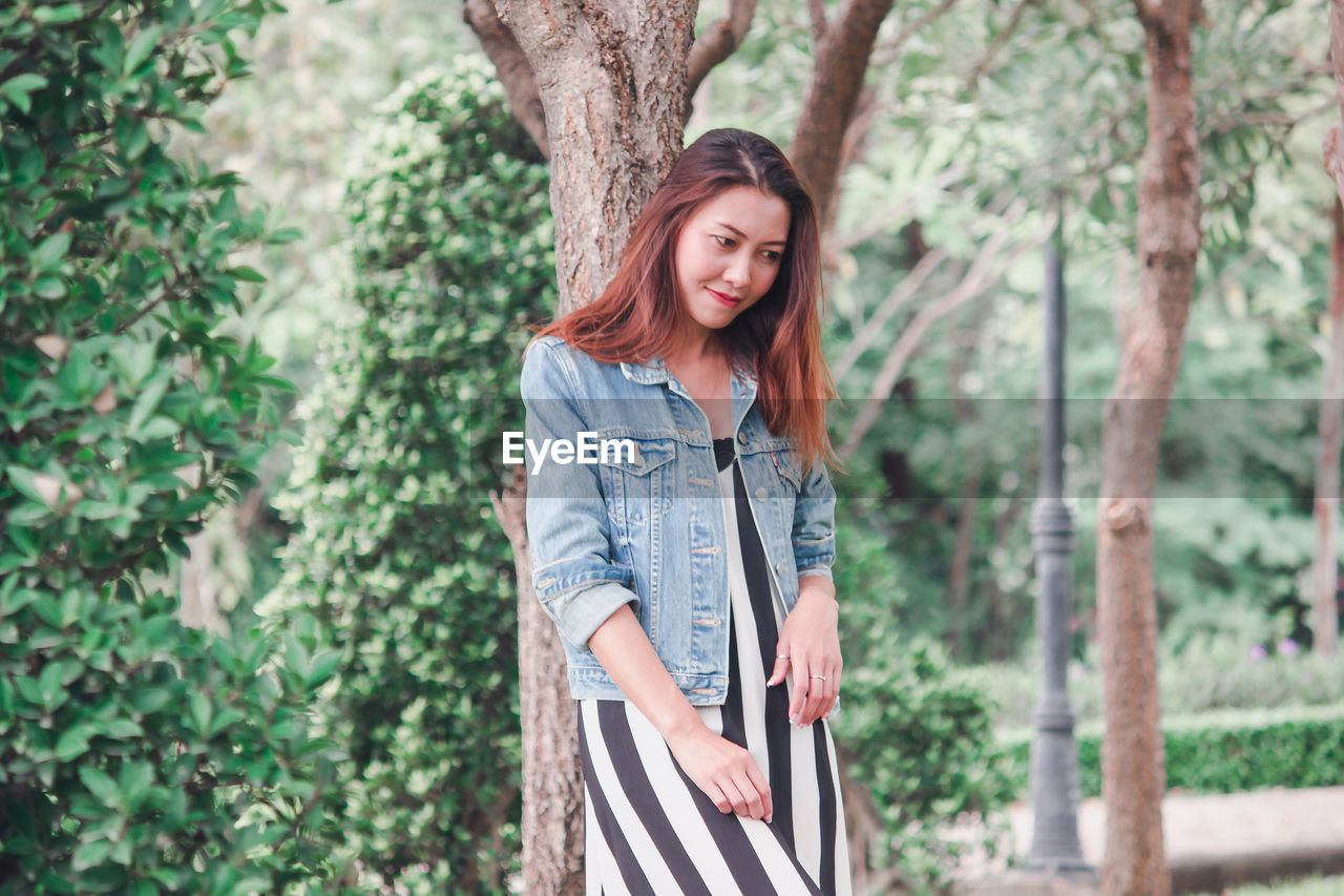 Smiling woman standing against tree trunk