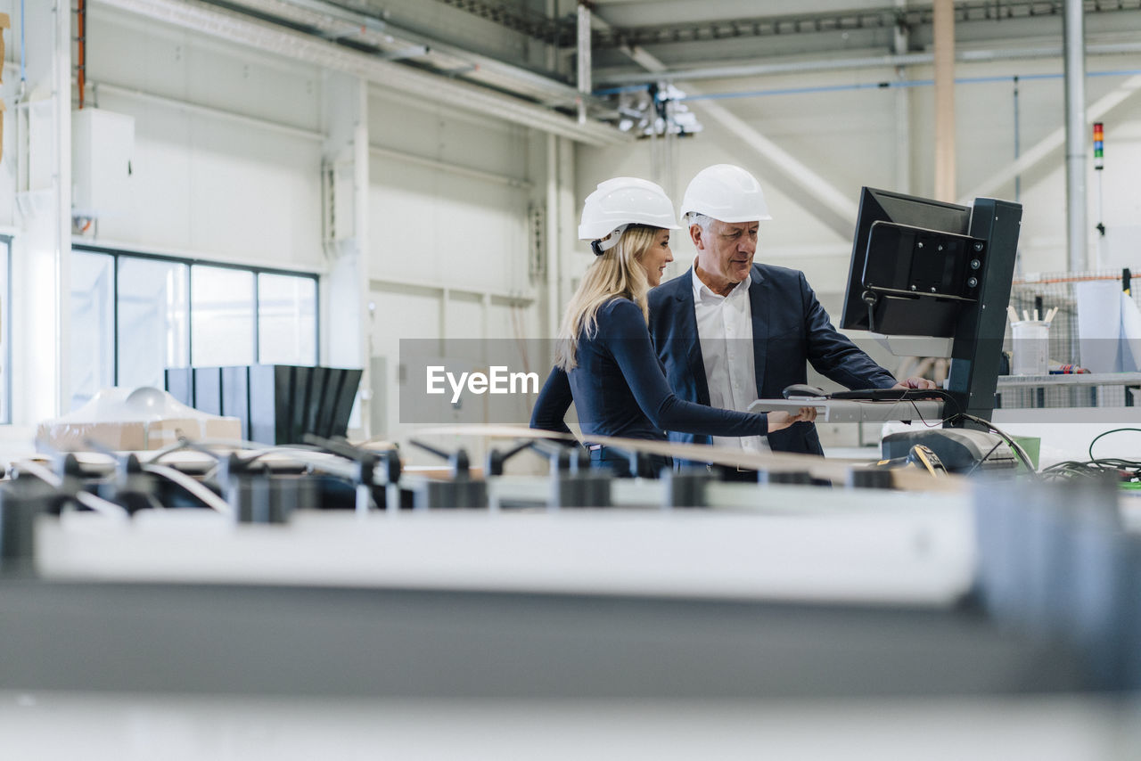 Businessman and colleague working on desktop pc in factory