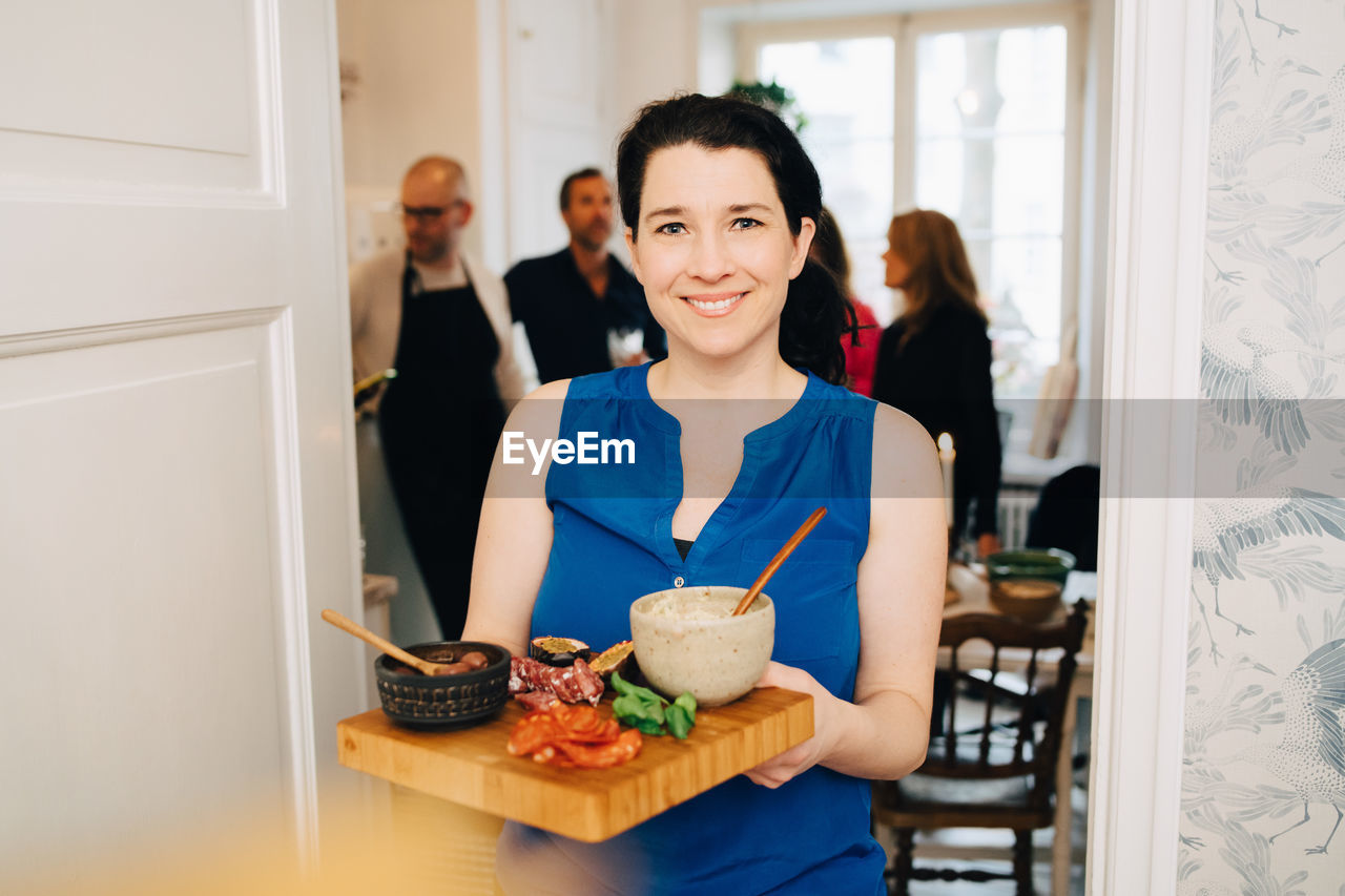 Portrait of smiling woman holding serving tray while standing at doorway in party