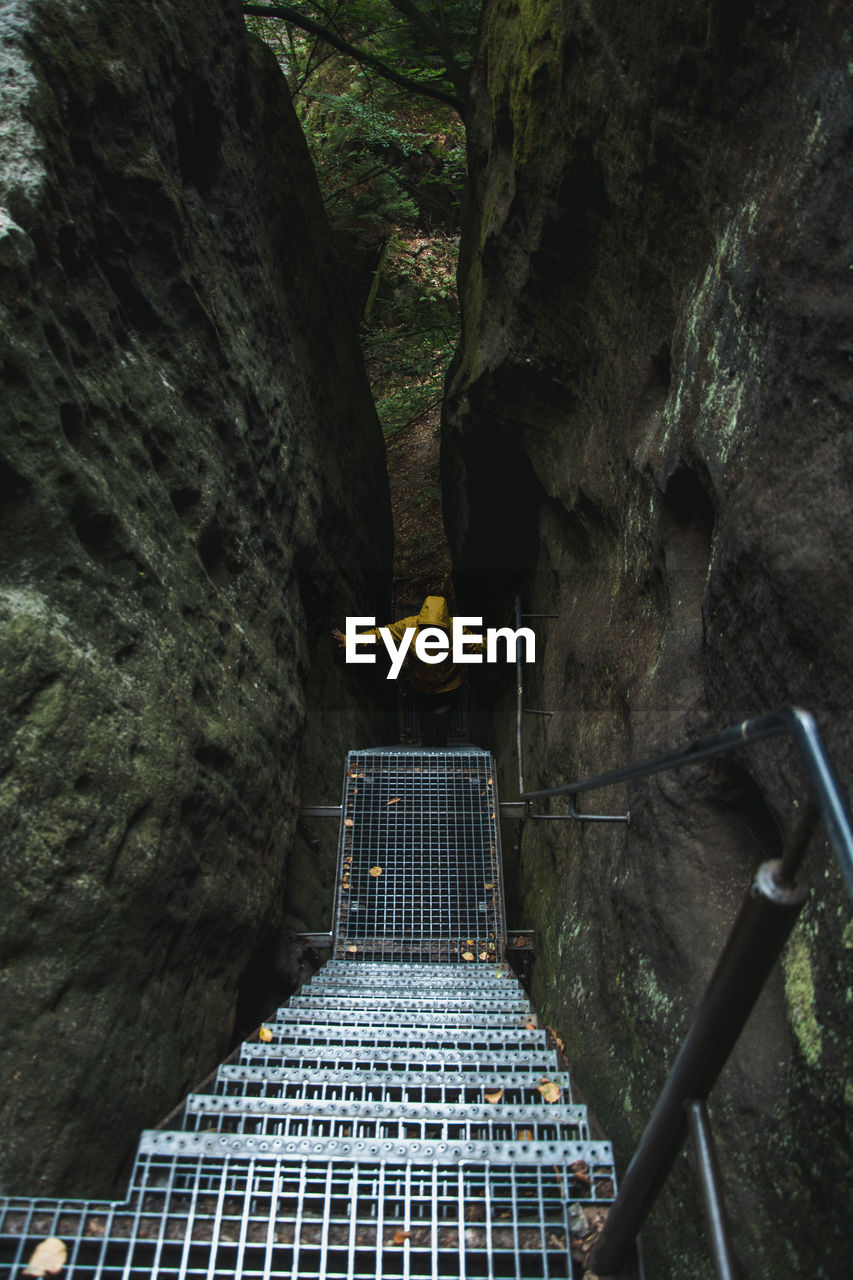 Hiker in yellow raincoat climbing up stairs amidst rocks