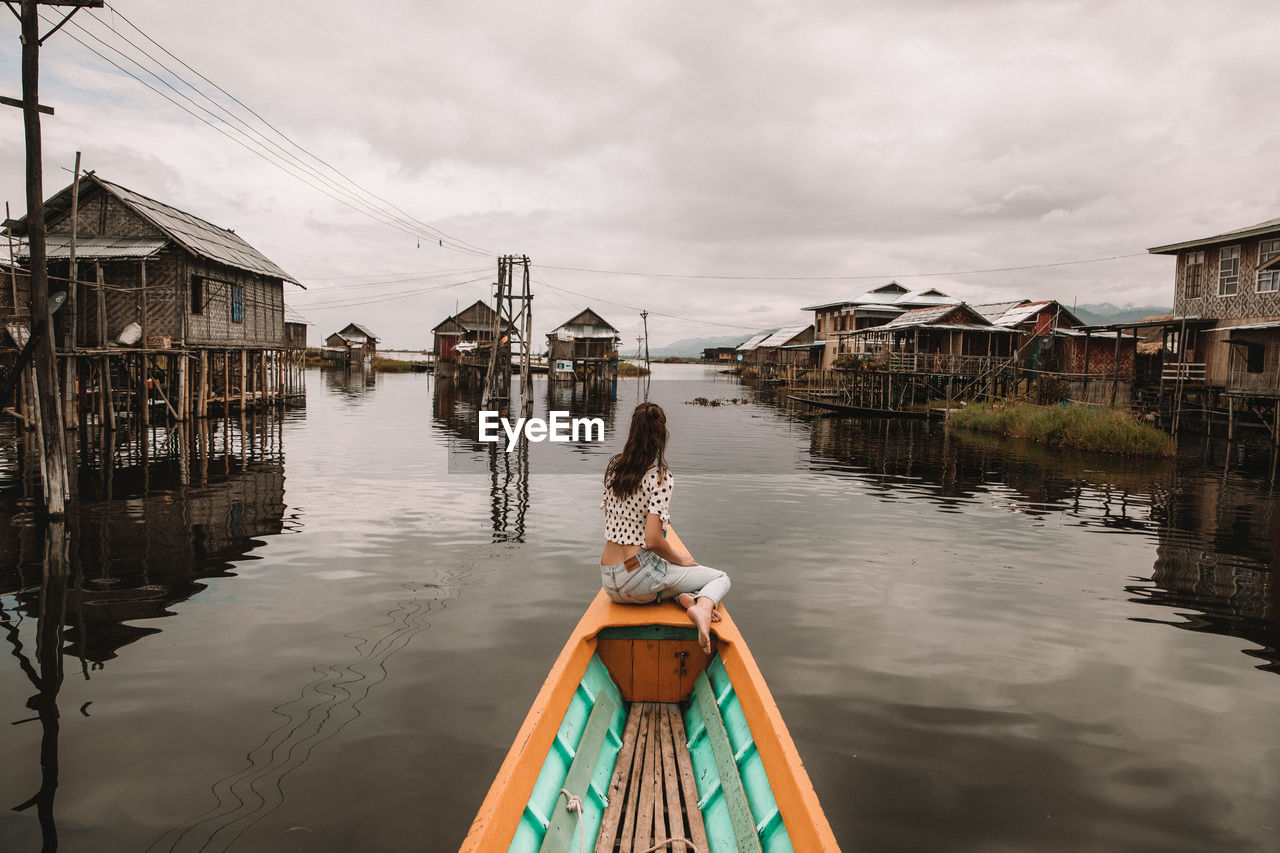 Woman sitting on boat in lake against houses
