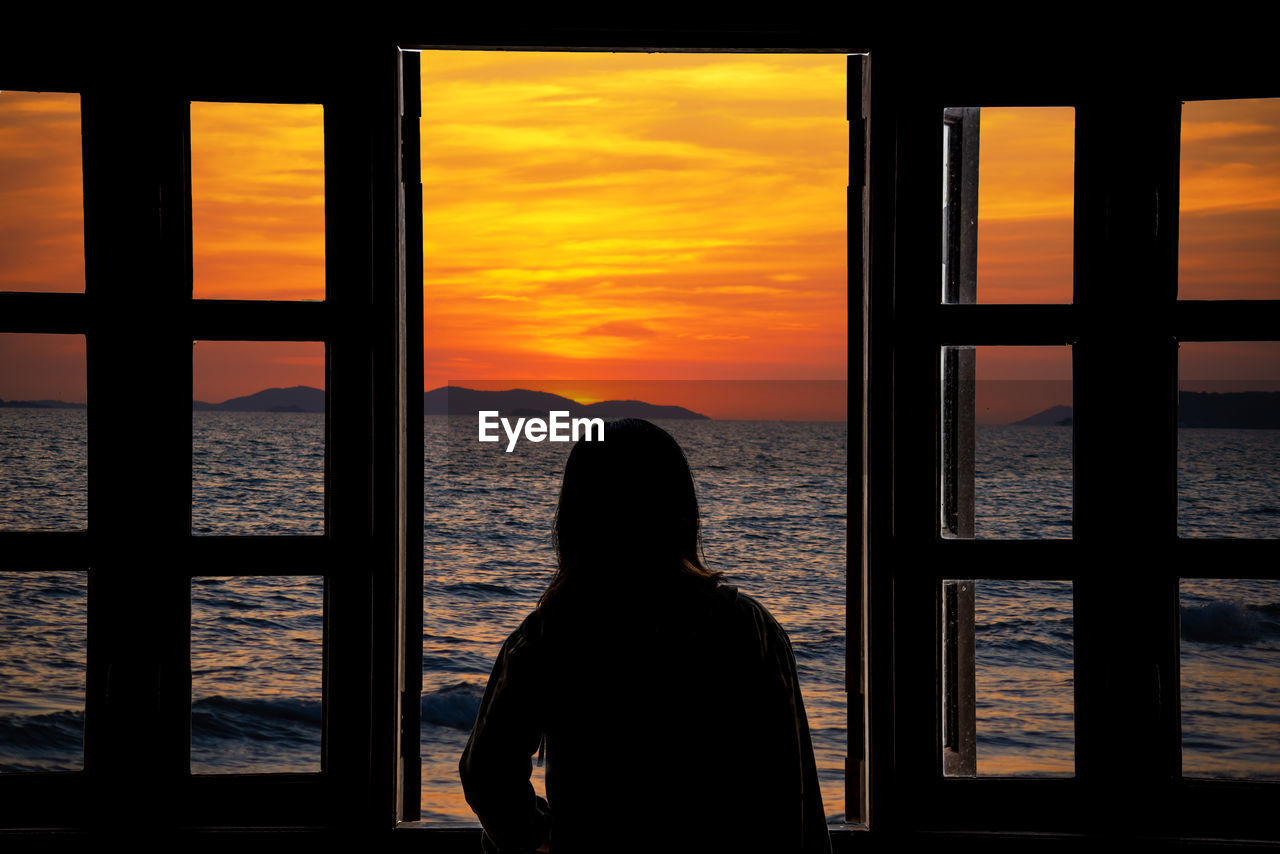 Rear view of silhouette woman looking at sea against sky during sunset