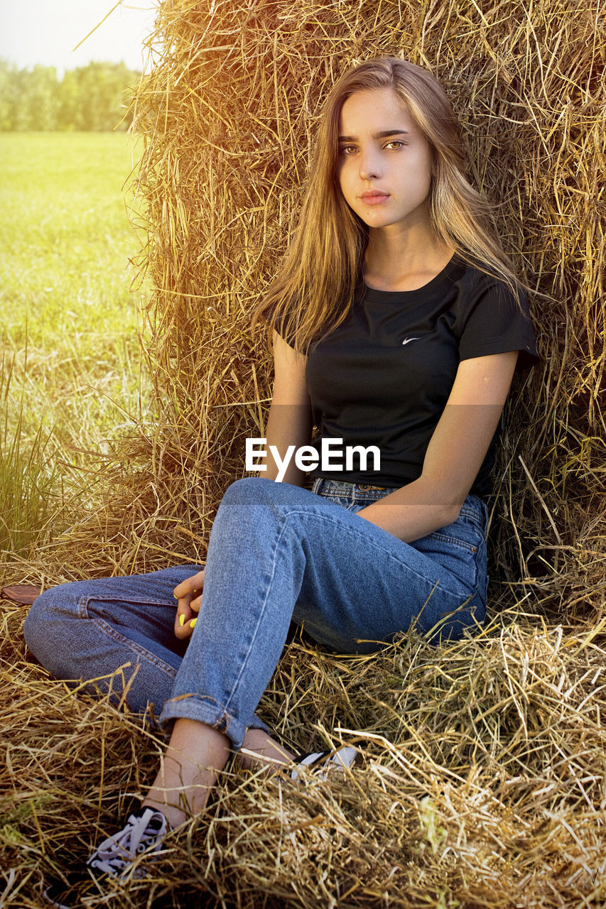 Portrait of young woman sitting against hay bale