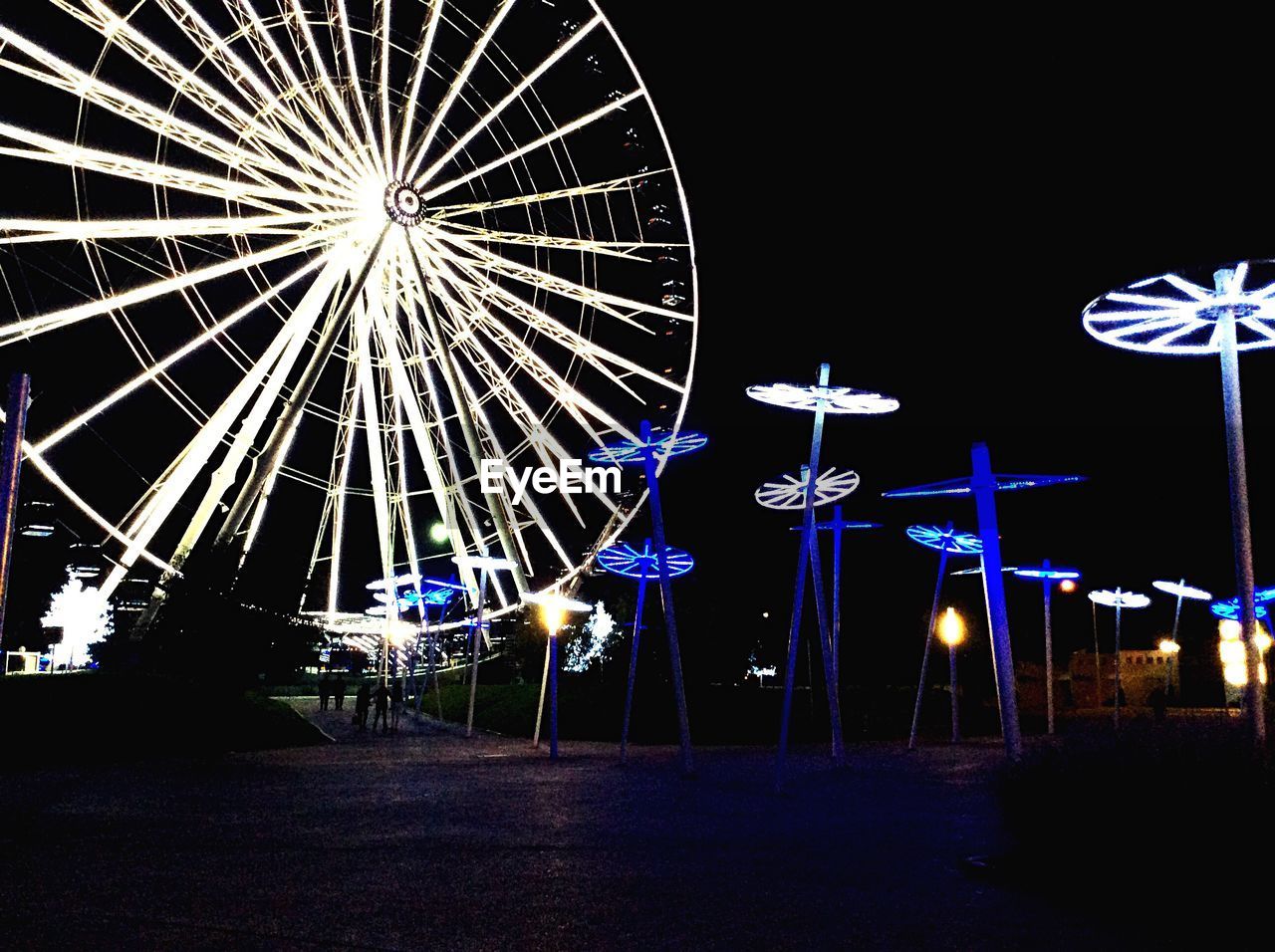 Illuminated ferris wheel in amusement park against clear sky at night