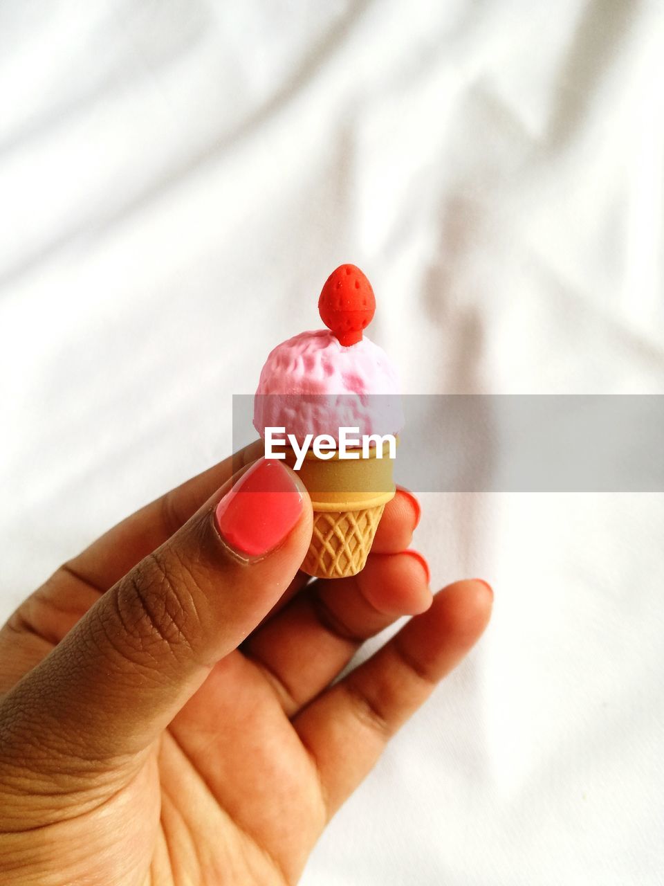 Cropped hand of woman holding small ice cream against white fabric