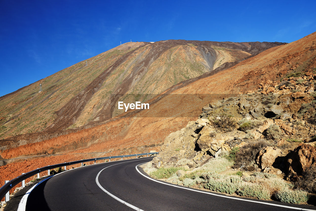 Empty road along rocky landscape against blue sky