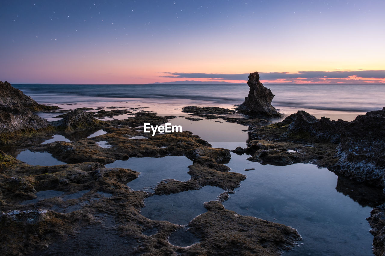 ROCK FORMATION ON SEA AGAINST SKY AT SUNSET