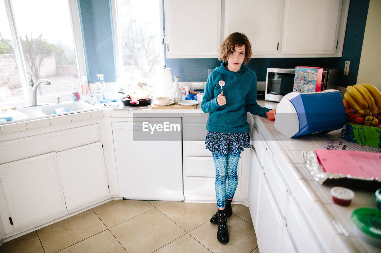 Girl in her kitchen looks toward camera annoyed