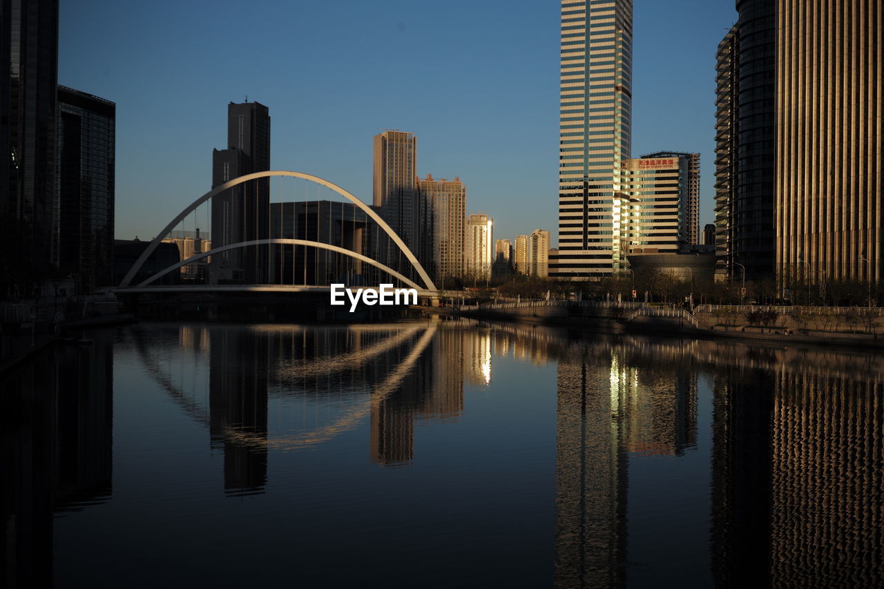 Reflection of buildings in city against clear sky