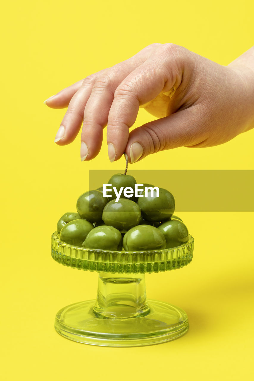 Woman's hand grabbing an olive by the tail from a  tray full of fresh green olives. stack of olives.