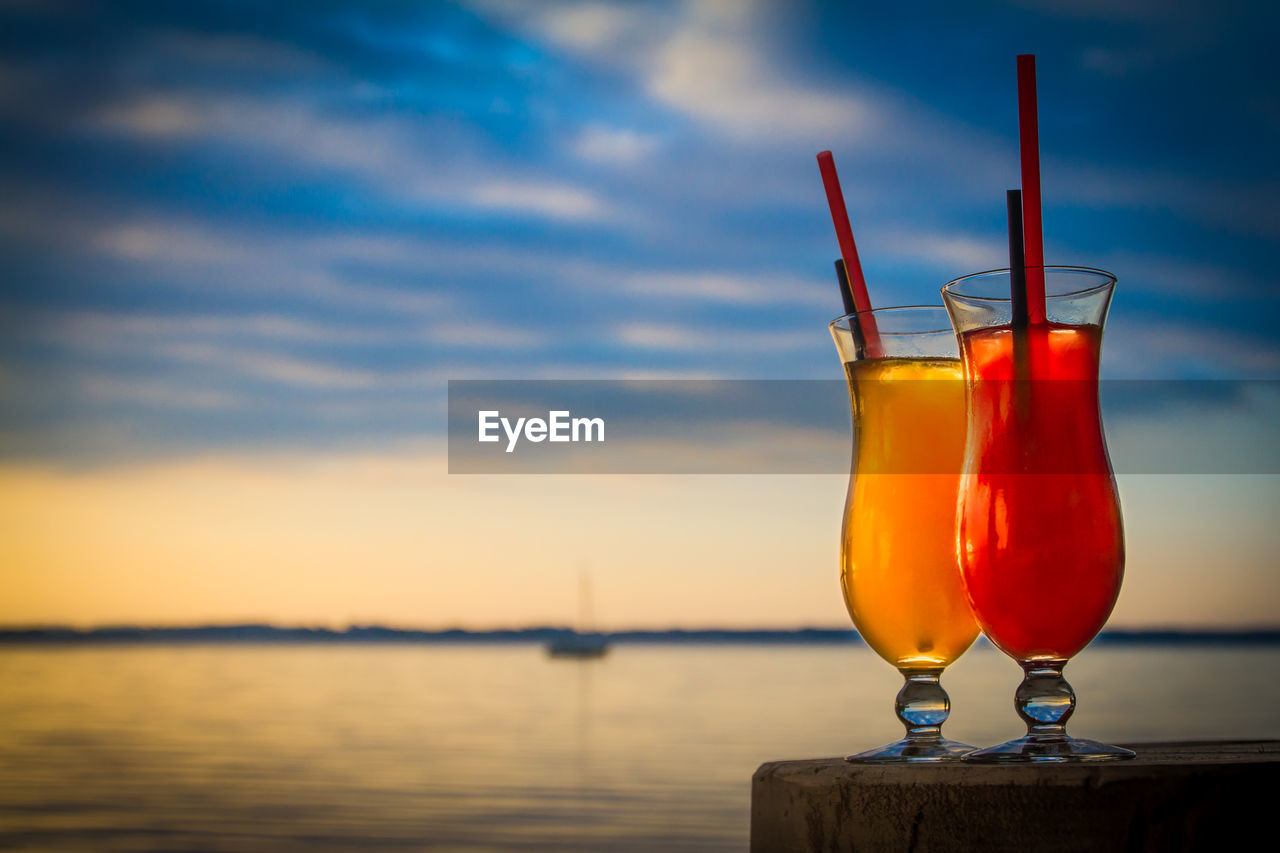Drinks on wood against sea during sunset