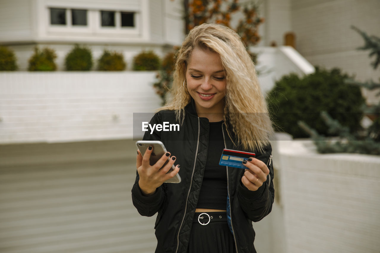 Smiling blond woman buying online through mobile phone and credit card