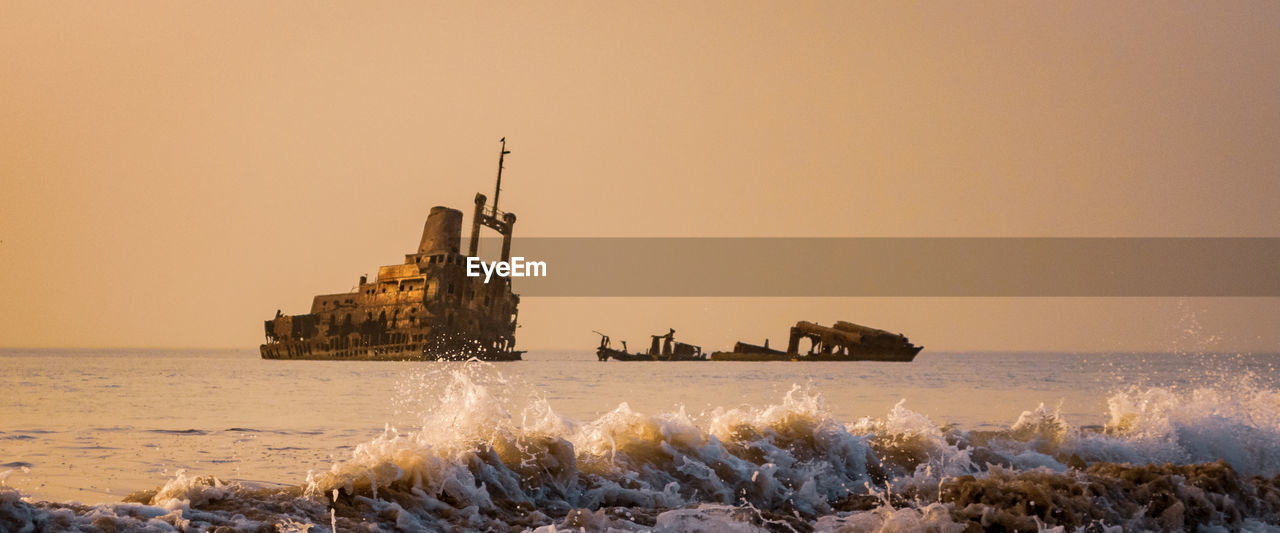 Scenic view of sea against clear sky during sunset with shipwreck
