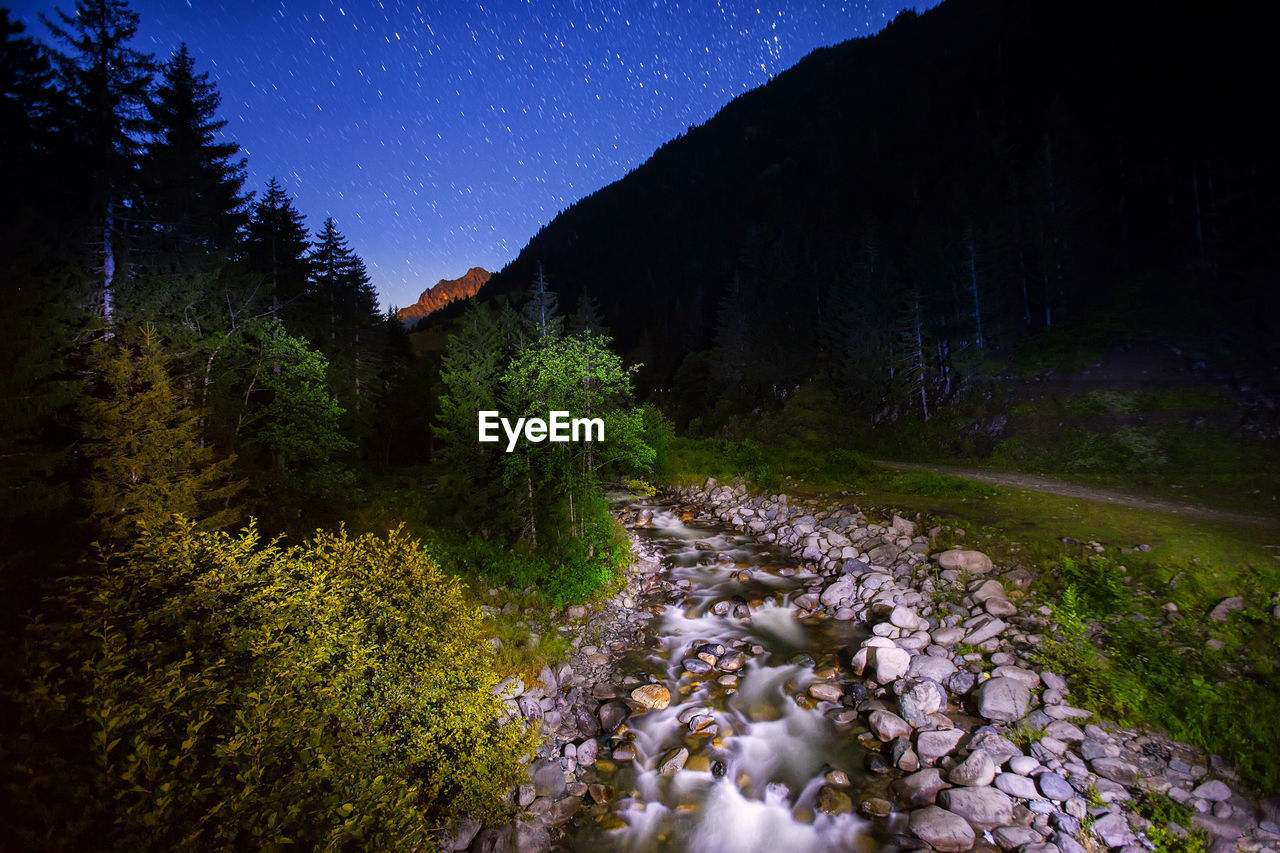 Stream flowing by mountain at night