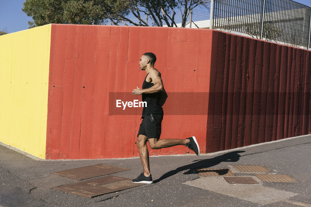 Full length of african american runner running against colorful wall person