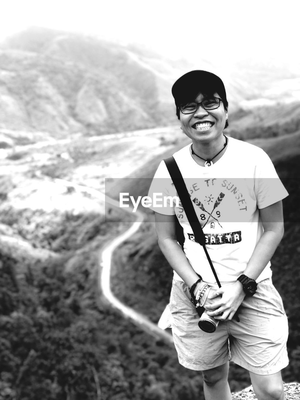 PORTRAIT OF SMILING YOUNG MAN STANDING ON MOUNTAIN