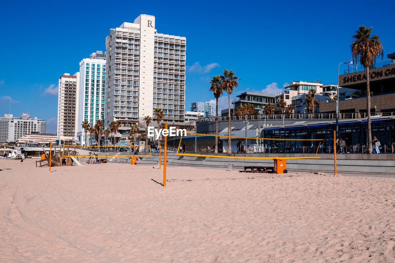 beach, architecture, built structure, building exterior, sky, city, boardwalk, land, sand, walkway, building, nature, travel destinations, office building exterior, blue, vacation, landscape, travel, sea, clear sky, skyscraper, tropical climate, water, sunny, outdoors, palm tree, day, cityscape, residential district, coast, no people, downtown, tree, trip, urban skyline, tourism, sunlight, holiday