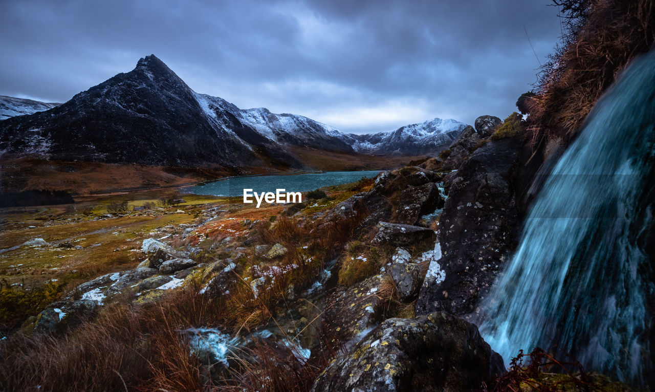 Scenic view of waterfall on mountains against sky