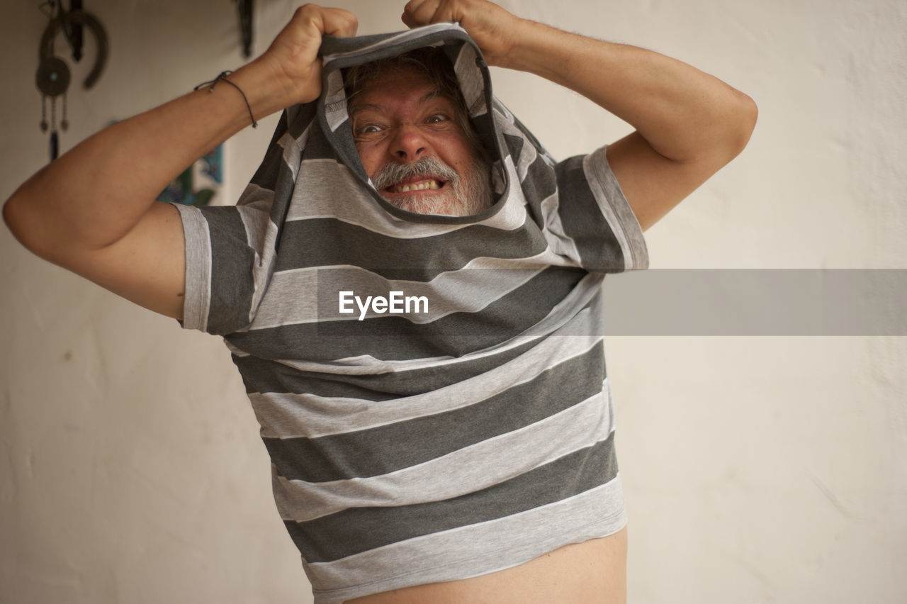 Senior man removing striped t-shirt at home