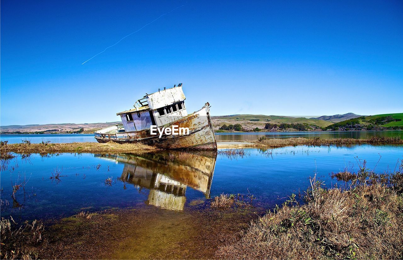 Abandoned boat on calm lake against clear blue sky