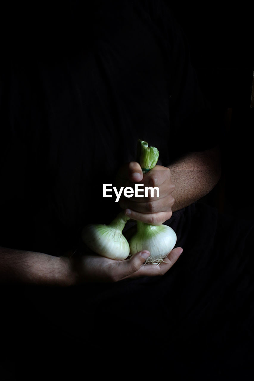 Close-up of hand holding fruit against black background