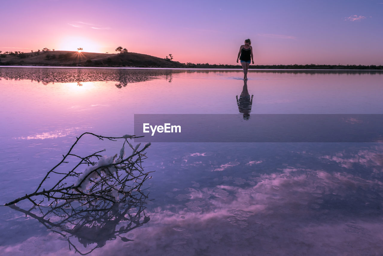 Woman walking in lake against sky during sunset