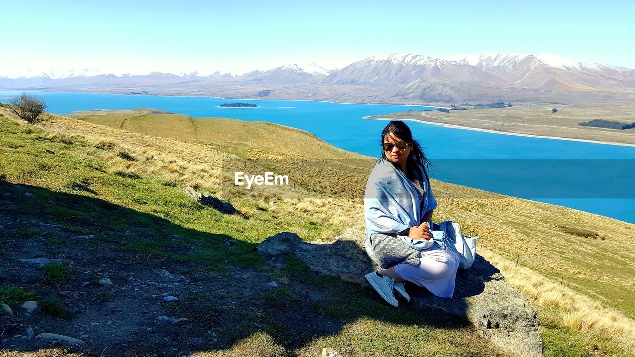 Woman sitting by lake on hill