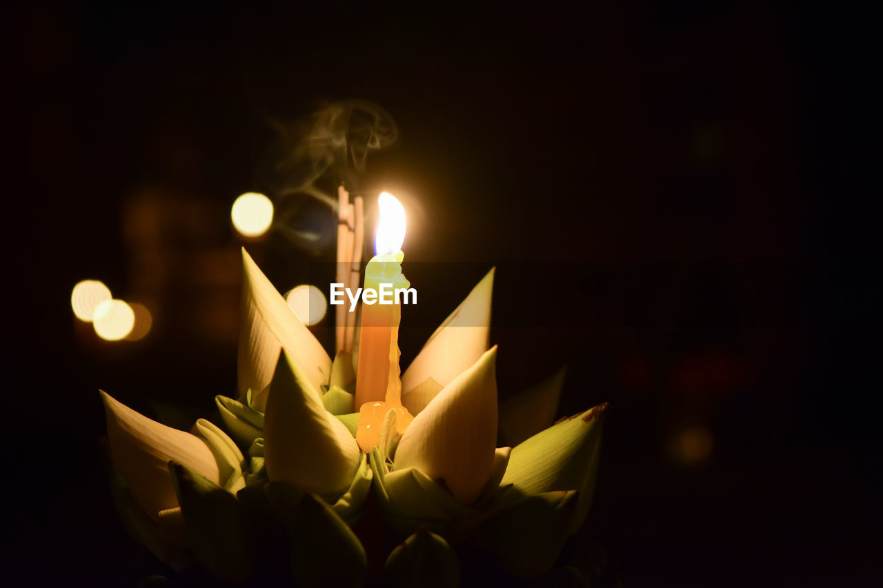 CLOSE-UP OF LIT CANDLES AGAINST DARK BACKGROUND